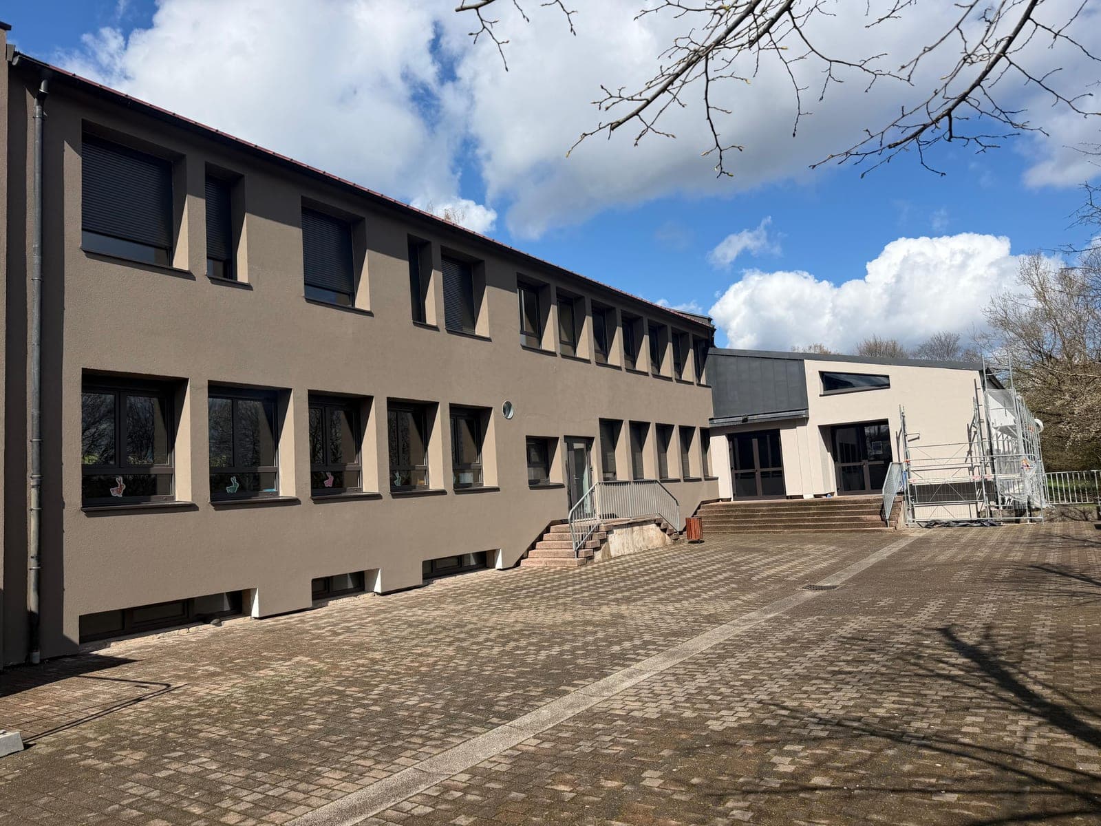 Après travaux : la même façade livrée en enduit taupe, encadrements de fenêtres crème, échafaudage démonté et cour pavée dégagée sous un ciel bleu.