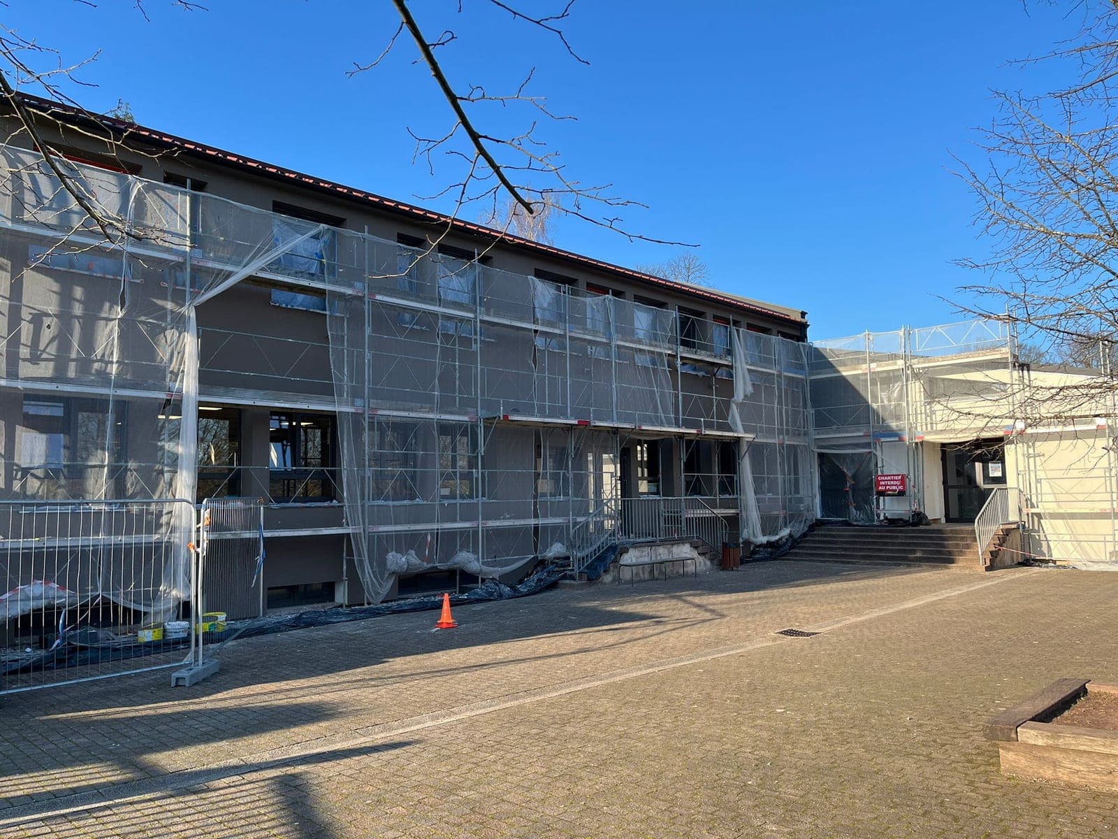 Avant travaux : la façade sur cour du collège entièrement masquée par un échafaudage et ses filets de protection, barrière de chantier et panneau « chantier interdit au public » devant l'entrée.