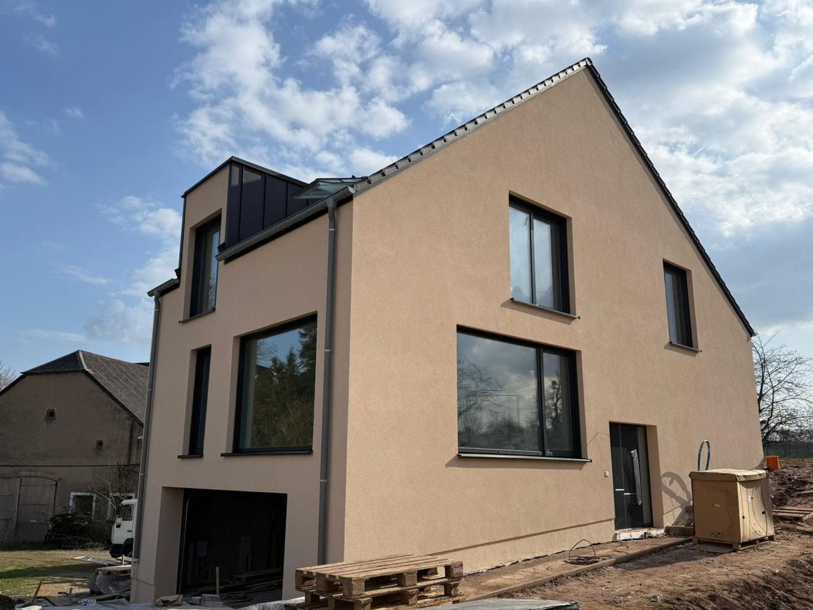 Maison individuelle neuve isolée par l'extérieur, enduit beige rosé et encadrements anthracite, vue de trois quarts sous un ciel dégagé